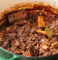 a green pot filled with meat and sauce on top of a table next to a wooden spoon