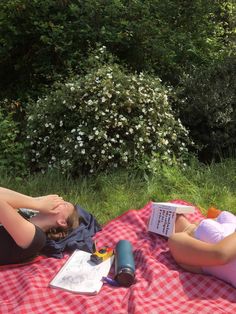 two women are laying on a blanket reading books and having fun with each other in the park