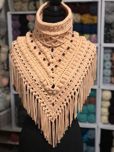 a crocheted shawl with fringes and beads is on a mannequin