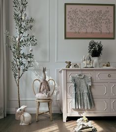 a baby's room with a white dresser, pink chair and stuffed animals on the floor