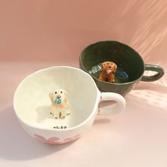 two mugs with dogs on them sitting next to each other in front of a pink background