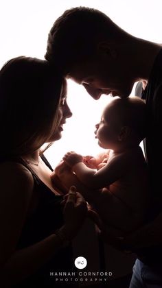 a man and woman holding a baby in front of a white background with the light coming through them