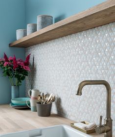 a kitchen sink and counter with flowers on the shelf next to it, in front of a tiled backsplash