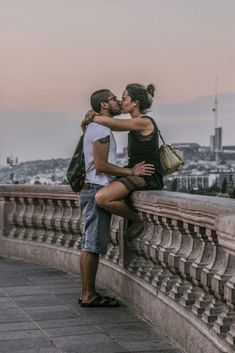 a man and woman kissing on the side of a bridge