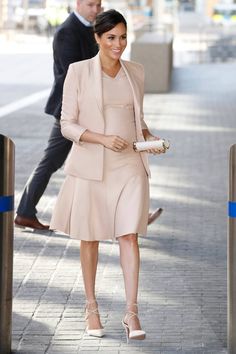 a woman in a dress and jacket is walking down the street with another man behind her