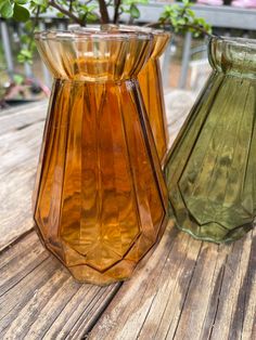 two glass vases sitting on top of a wooden table next to eachother