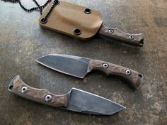 two knives are laying next to each other on a table with a chain and pouch