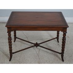 an old wooden table with roped legs and a square top on concrete flooring