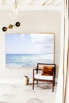 a painting hangs on the wall next to a chair in front of an ocean scene