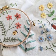 a close up of a cross stitch pattern with flowers and bugs on the fabric next to it