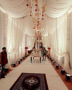 a man and woman standing in front of a white wedding ceremony aisle with chandelier hanging from the ceiling