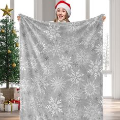 a woman in a santa hat is holding up a gray and white snowflake blanket