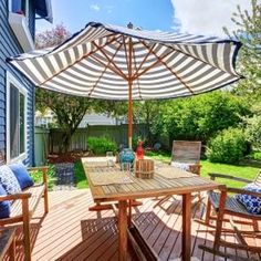 an outdoor table and chairs on a wooden deck with an umbrella over the dining area