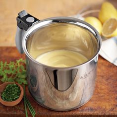 a silver pot filled with liquid next to some lemons and parsley on a cutting board