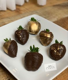 four chocolate covered strawberries on a white plate with gold foiled decorations around them