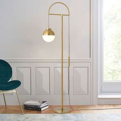 the floor lamp is next to a blue chair and book on the floor in front of a white wall