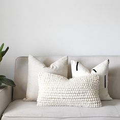 a white couch with two pillows and a potted plant next to it on the side