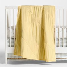 a baby crib with a yellow blanket hanging from it's side, and a white crib in the background