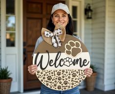 a woman holding a welcome sign in front of a house with her dog's paw on it