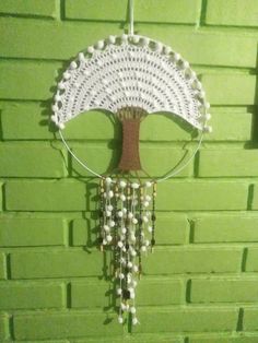 a crocheted umbrella hanging on the side of a green brick wall with beads