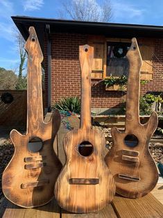 three guitars made out of wood sitting on top of a wooden table in front of a house