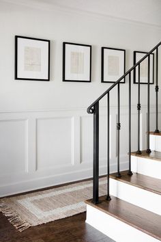 three framed pictures hang on the wall next to a stair case in a white room