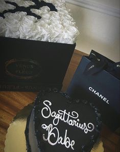 a black heart shaped cake sitting on top of a table next to a box of white roses