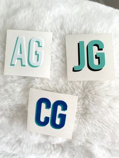 three stickers with the letters jg and g are on top of a fluffy white blanket