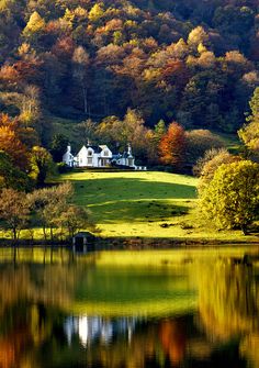 a house sits on the side of a hill overlooking a lake with trees around it