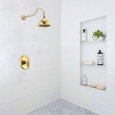 a white tiled bathroom with gold fixtures and shelving on the wall, along with shelves