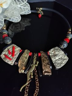 Beautiful modern style choker necklace with an ethnic touch. The necklace is made of large irregular flakes of agate and bone stone galvanized in gold, lava stone, red coral and hematite. The central part of the necklace is made with rather large stones which make the necklace very eye-catching. This necklace is the fruit of my imagination, it is an artistic jewel created with various natural stones and crystals. The necklace is rigid but rests naturally on the neck, very comfortable to wear. The back is made with silicone cord. The necklace is very bright, 47cm long with an adjustable hook clasp. The necklace is in shades of gold, black, and red which make it very elegant. It is a particular necklace, for those who love handmade pieces. The necklace is very elegant, very beautiful in summ Unique Choker Necklace With Natural Stones, Unique Red Stone Necklaces, Bohemian Gold Necklace With Stones, Gold Metal Jewelry With Gemstone Beads, Unique Red Brass Necklaces, Unique Red Brass Necklace, Gold Beaded Choker With Natural Stones, Bohemian Gold Choker With Natural Stones, Unique Metal Necklace With Natural Stones