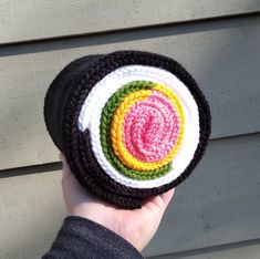 a person holding up a crocheted hat in front of a wooden wall