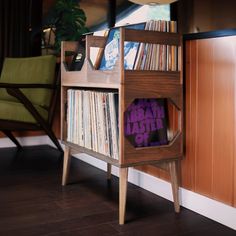 a wooden shelf with various records on it and a green chair in the back ground