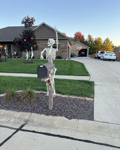 a skeleton mailbox sitting on the side of a road in front of a house