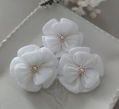 three white flowers with pearls on them sitting on a plate