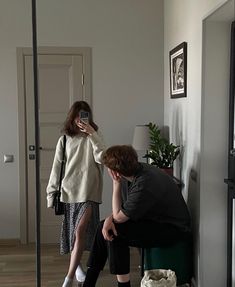 a man taking a picture of a woman in the mirror with her cell phone while sitting on a chair