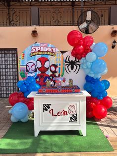 a table topped with balloons and a spiderman cake on top of a green carpet