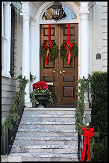 two wreaths on the front steps of a house decorated for christmas with red bows