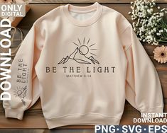 a white sweatshirt with the words be the light on it next to flowers and a potted plant