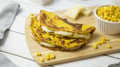 some food is sitting on a cutting board next to a bowl of corn and cheese