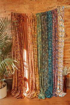 an assortment of different colored curtains hanging on a brick wall next to a potted plant