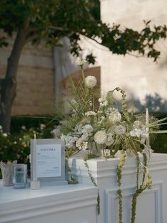 a table with flowers and cards on it in front of a tree, next to a building