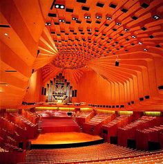 an auditorium with rows of seats and a large pipe organ in the center is lit by red lights