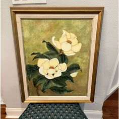 an oil painting of white flowers in a gold frame sitting on a black stool next to a wall