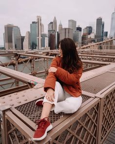 a woman sitting on the edge of a bridge in front of a cityscape