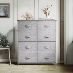 a white and grey dresser with drawers in a living room next to a plant on a table