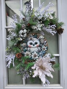 a wreath with an owl and pine cones is hanging on a window sill next to flowers