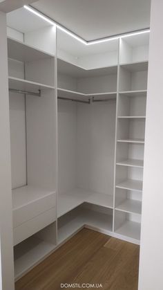 an empty walk in closet with white shelving and wooden flooring on the side