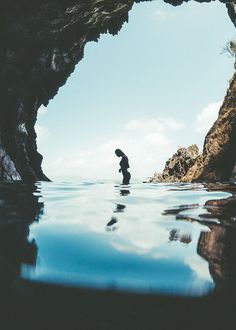 a person standing in the water with an umbrella near some rocks and another body of water