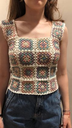 a woman is wearing a crocheted top and denim shorts with her hands in her pockets